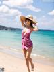 A woman in a pink dress and hat on the beach.