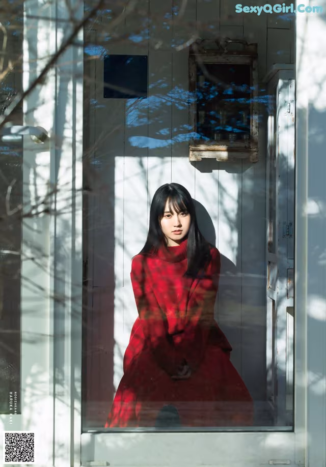 A woman in a red dress is looking out of a window.