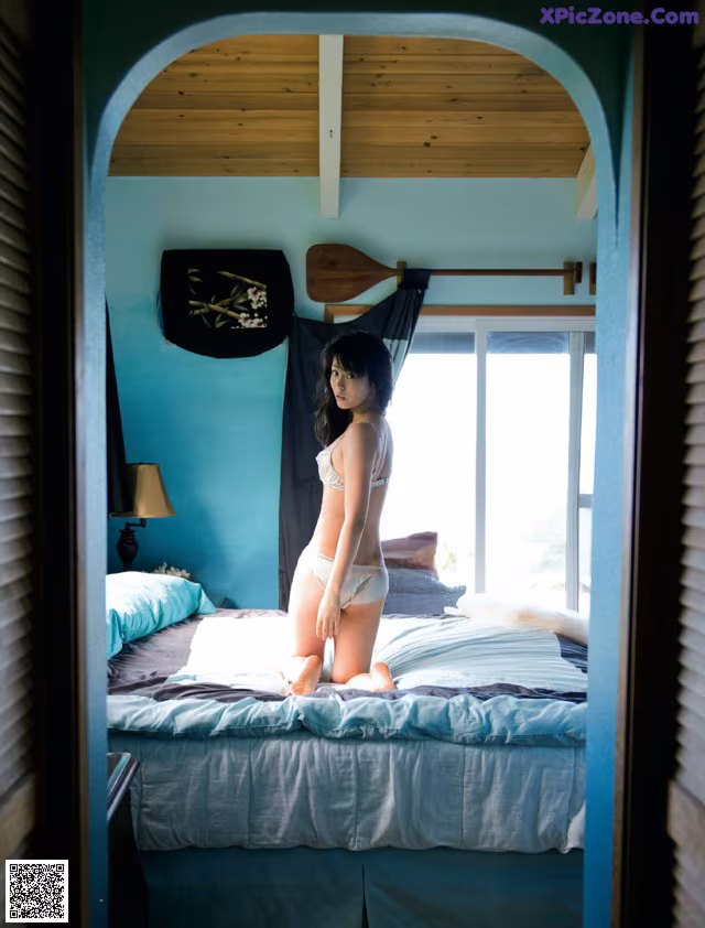 A woman in a white bikini sitting on a bed.