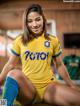 A woman in a yellow and blue soccer uniform sitting on the ground.