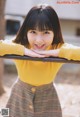 A young woman in a yellow sweater leaning on a railing.