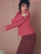 A woman in a pink jacket and plaid skirt posing for a magazine.