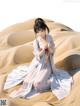 A woman in a white dress sitting on a sand dune.