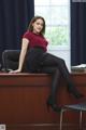 A woman sitting on top of a desk next to a chair.