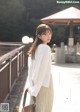 A woman in a white sweater and pleated skirt holding a brown bag.