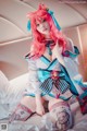 A woman with pink hair sitting on a bed.